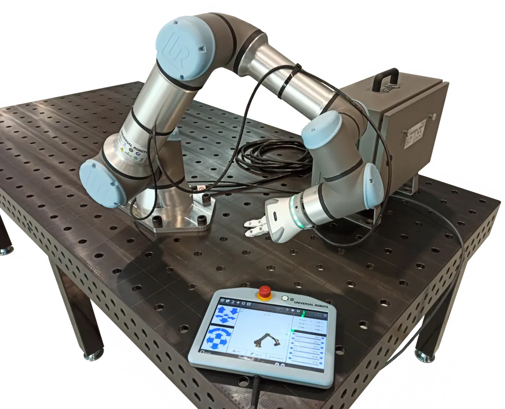 A Universal Robots UR16e collaborative robot arm mounted on a fixturing table, with its gray controller box behind it and a teach pendant showing the robot's joint positions and an emergency-stop button in the foreground.