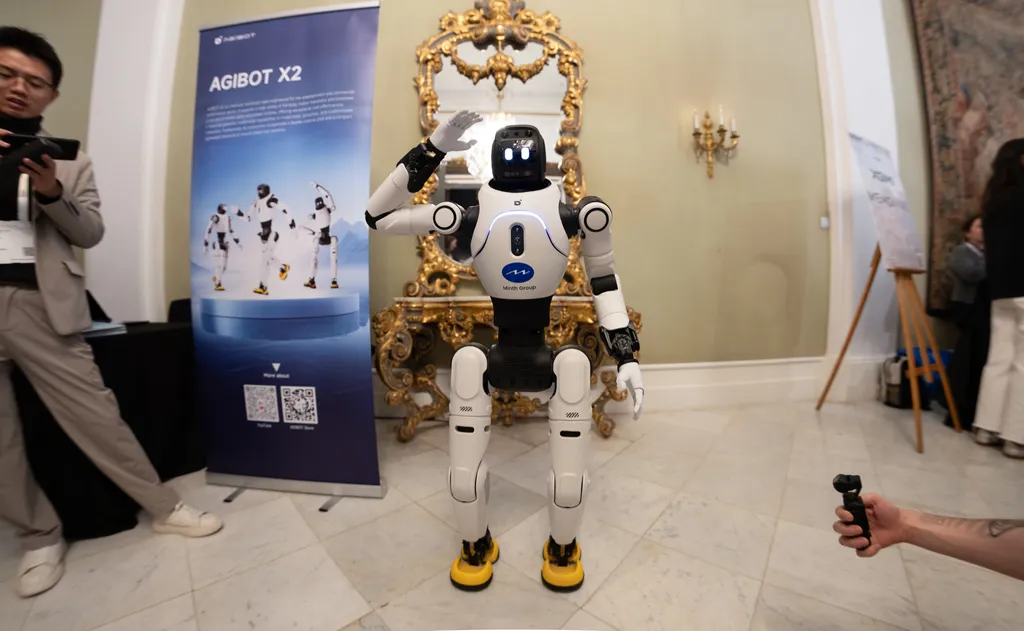 AGIBOT's X2 humanoid robot, a white and dark bipedal robot with a rounded head and slim torso, standing on display at a trade-show booth.