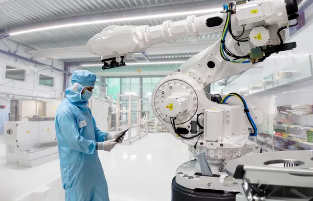 A field service engineer in a full cleanroom suit stands with a tablet beside a large white ABB IRB 7600 six-axis industrial robot arm inside an ISO 14644-1 Class 6 cleanroom.