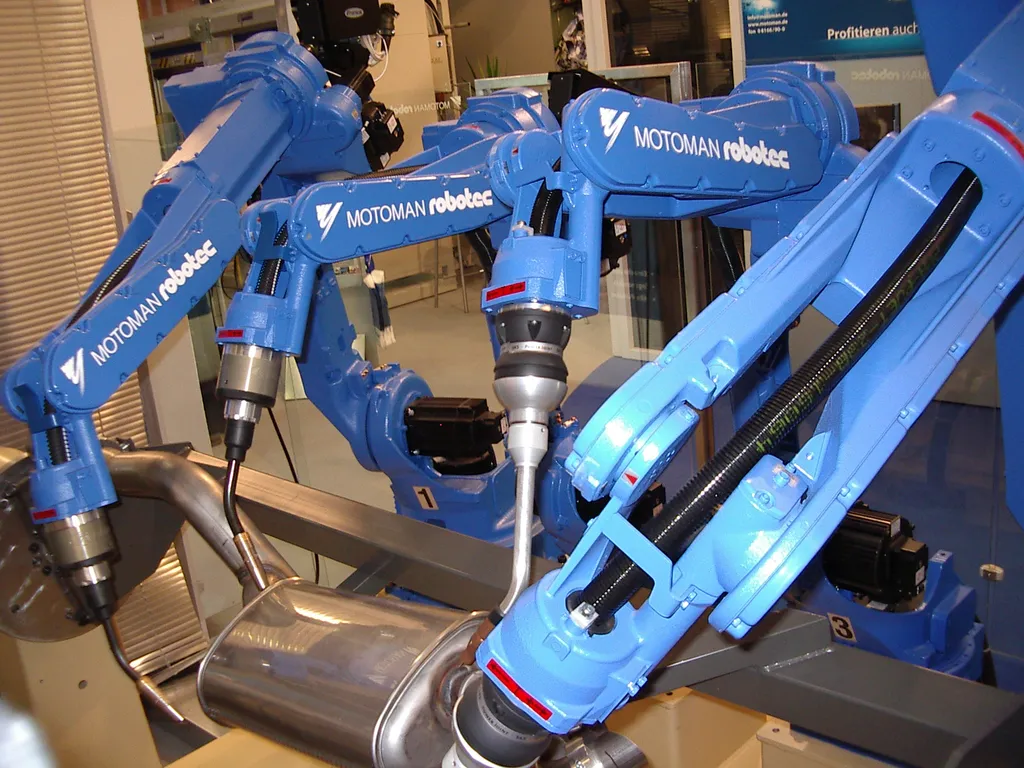 Several blue Yaskawa Motoman industrial welding robot arms, branded 'MOTOMAN robotec,' displayed side by side on a showroom floor.