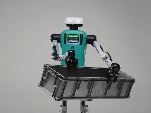 Agility Robotics' Digit humanoid — a bipedal robot with a teal torso, a white LED face panel and articulated black-and-silver arms — carries a large gray warehouse tote against a plain studio backdrop.